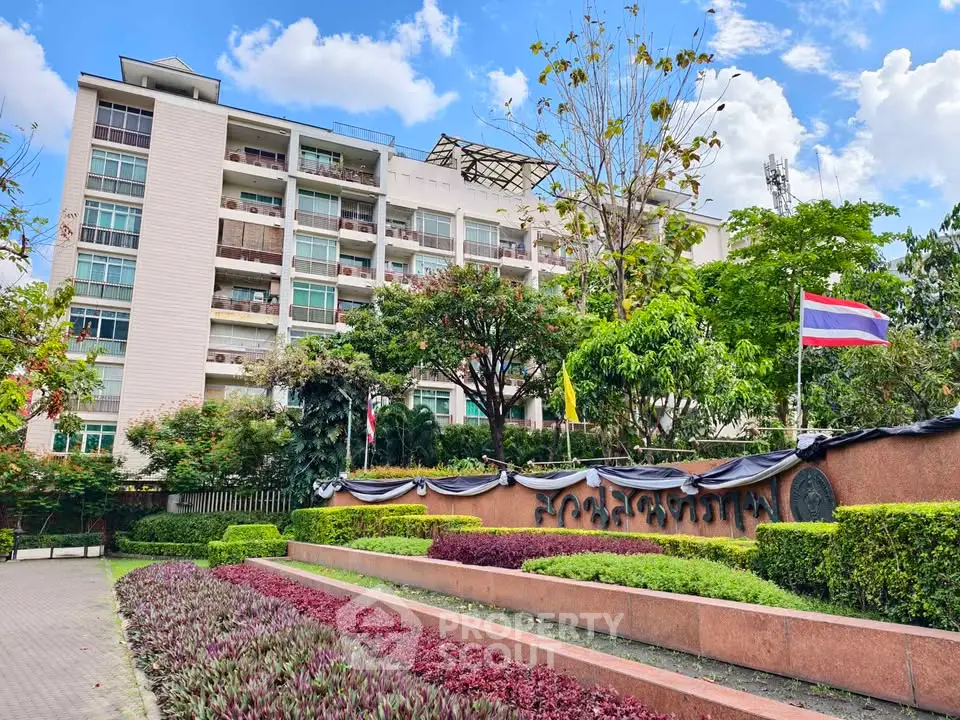Modern apartment building with lush garden and national flags in vibrant urban setting.
