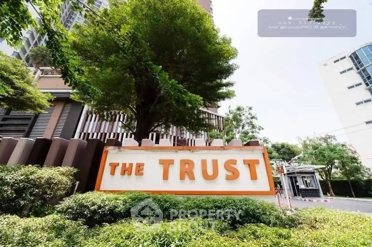Modern condominium entrance with lush greenery and prominent signage at The Trust.