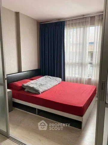 Cozy bedroom with red bedding and large window, perfect for relaxation.