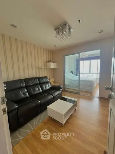 Cozy living room with black leather sofa and view into bedroom
