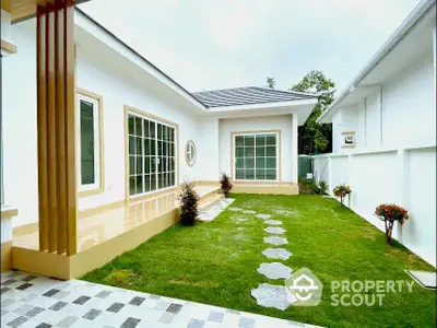 Charming single-story home with lush green lawn and modern design, featuring large windows and a cozy garden path.