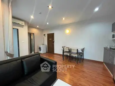 Modern living room with dining area and washing machine, featuring wood flooring and contemporary lighting.