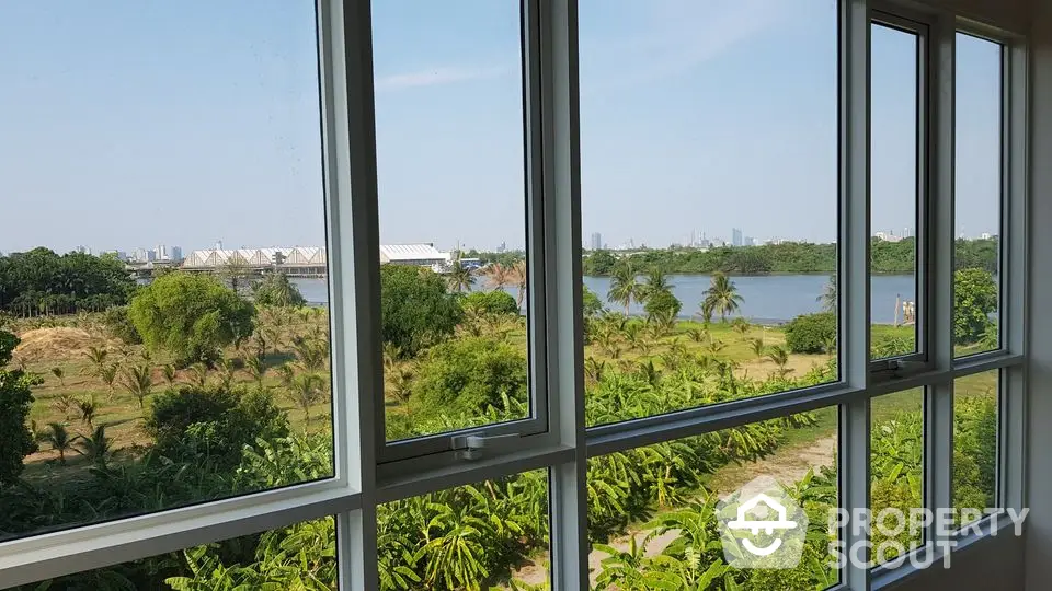 Stunning river view from modern apartment window, lush greenery and city skyline in the distance.