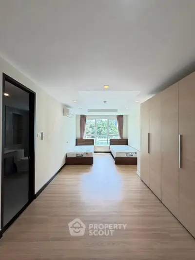 Spacious bedroom with twin beds and large wardrobe, featuring a bright window view.