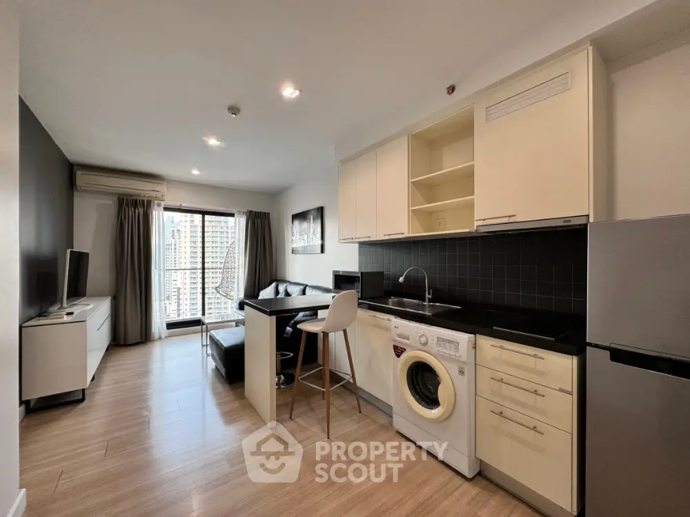Modern open-plan living room with kitchen featuring washing machine and city view balcony.