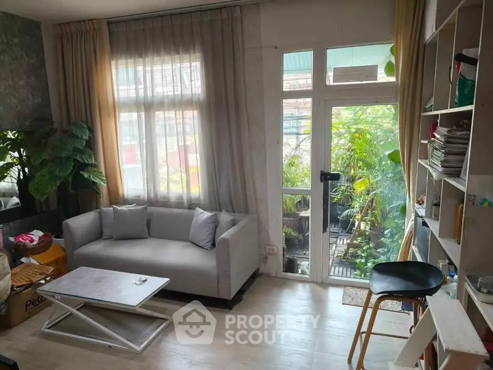 Cozy living room with large windows and balcony access, featuring modern furniture and lush greenery.