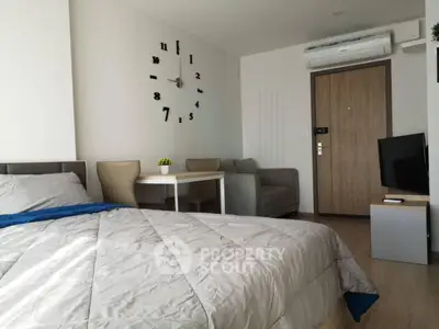 Modern studio apartment with cozy bed, stylish wall clock, and compact dining area.