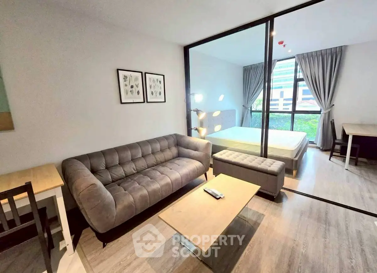 Modern studio apartment with stylish living area and bedroom, featuring sleek furniture and large windows.