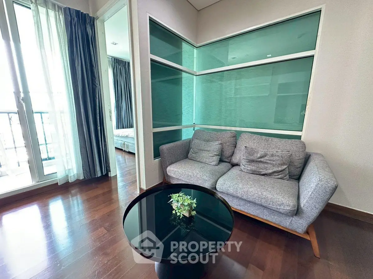 Modern living room with stylish sofa and glass coffee table, adjacent to a bright bedroom with balcony access.