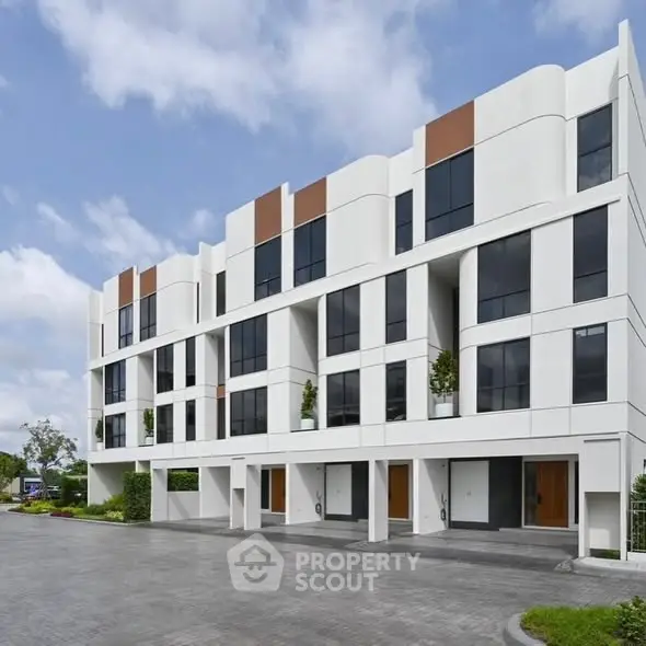 Modern multi-story building with sleek design and spacious parking area, ideal for urban living.