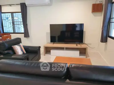 Modern living room with sleek black leather sofas and large flat-screen TV.
