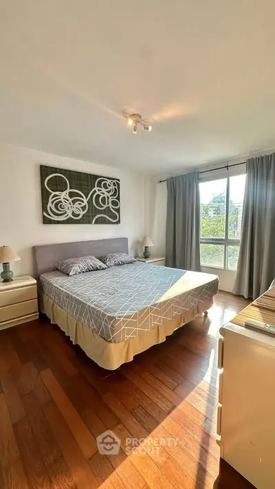 Spacious bedroom with large window and stylish decor, featuring hardwood floors and modern furnishings.