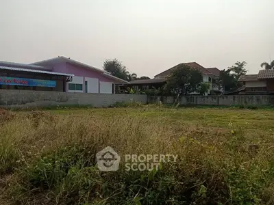 Spacious plot of land with residential buildings in the background, ideal for development.
