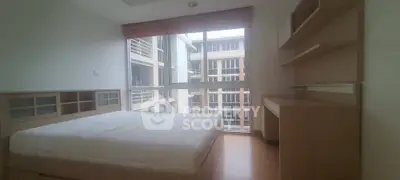 Spacious bedroom with large windows offering ample natural light and a serene view, complemented by built-in wooden shelving and a comfortable bed.