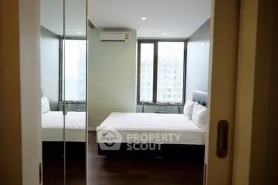 Spacious bedroom with mirrored closet and large windows offering city views.