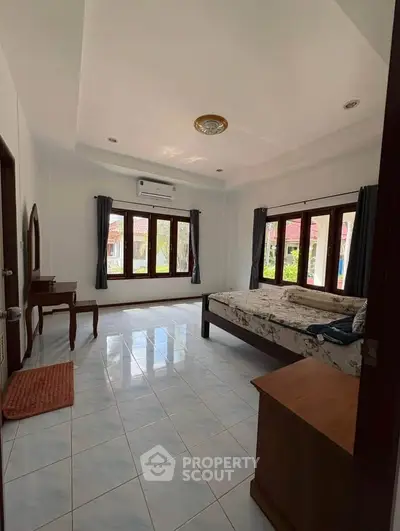 Spacious bedroom with large windows and natural light, featuring tiled floors and modern furnishings.