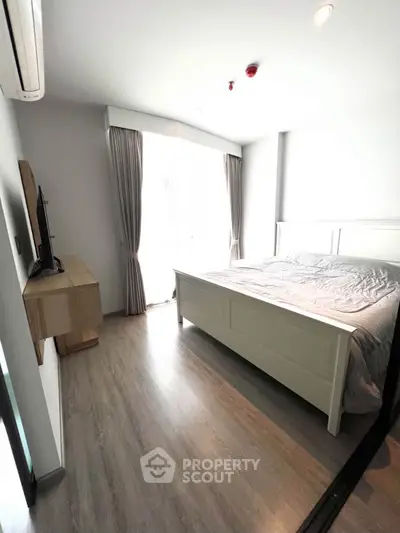 Modern bedroom with natural light, featuring a stylish bed and sleek wooden flooring.
