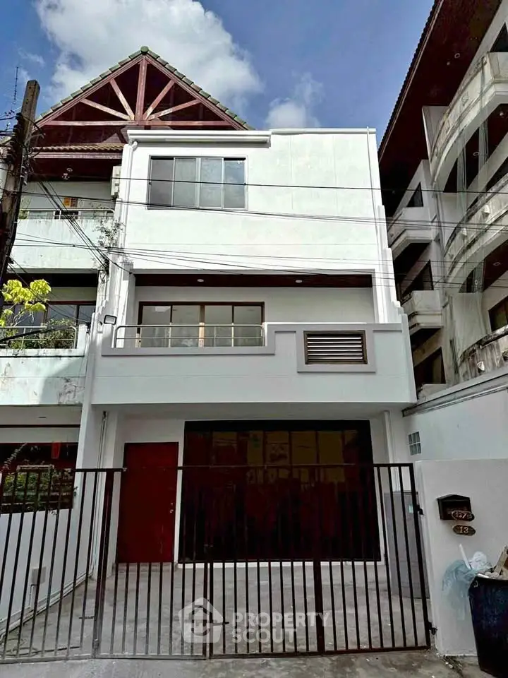 Modern three-story townhouse with gated entrance and balcony in urban setting.