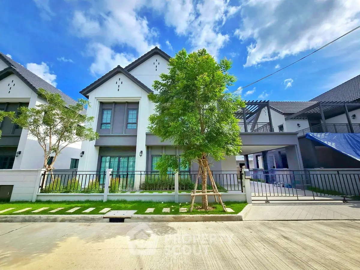 Modern two-story house with lush garden and spacious driveway under clear blue sky.
