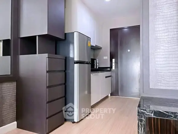 Modern kitchen with sleek cabinets and stainless steel fridge in compact apartment.