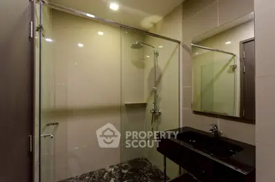Modern bathroom with glass shower and sleek black sink in contemporary apartment.