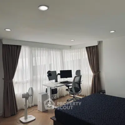 Modern bedroom with study area featuring sleek desk and ergonomic chair by large windows.