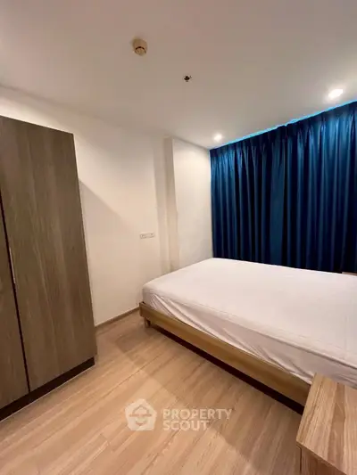 Cozy bedroom with wooden flooring and blue curtains, featuring a comfortable bed and wardrobe.