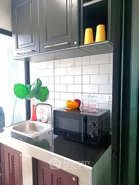 Modern kitchen with sleek black cabinets, microwave, and stylish backsplash.