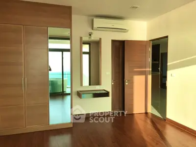 Spacious bedroom with wooden flooring and built-in wardrobe, featuring a balcony with ocean view.
