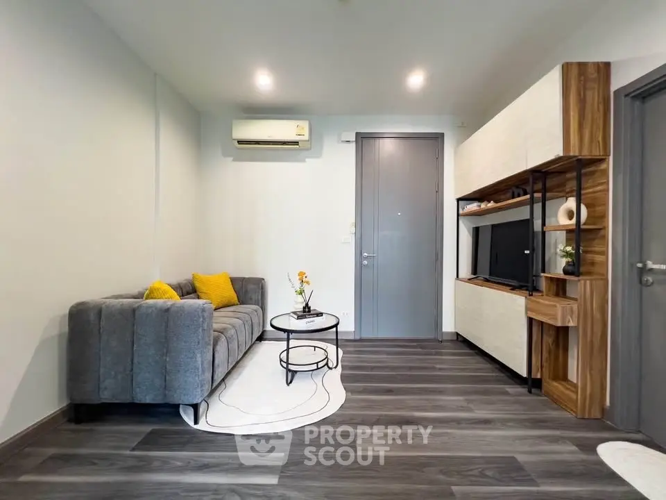 Modern living room with stylish gray sofa, wall-mounted TV, and sleek wooden flooring.