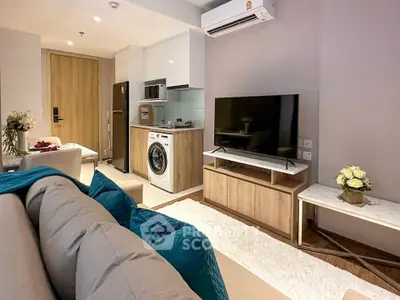 Modern living room with stylish furniture, TV, and compact kitchen featuring washing machine and microwave.