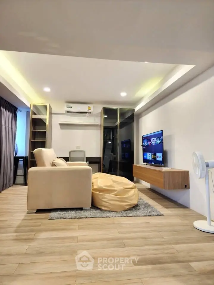 Modern living room with cozy seating and wall-mounted TV, featuring sleek wooden flooring and ambient lighting.