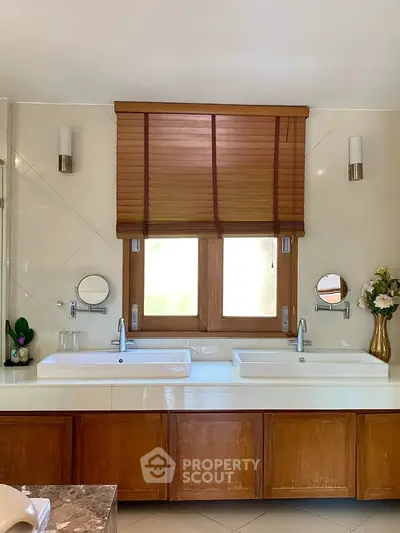 Elegant bathroom with dual sinks, wooden cabinetry, and stylish window blinds.