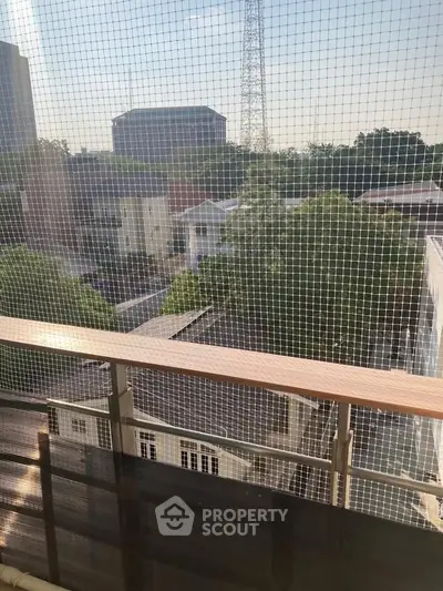Spacious balcony with safety netting offering a serene view of lush greenery and distant buildings.