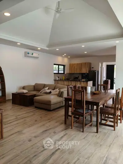 Spacious open-plan living room with modern kitchen and wooden dining set, perfect for family gatherings.