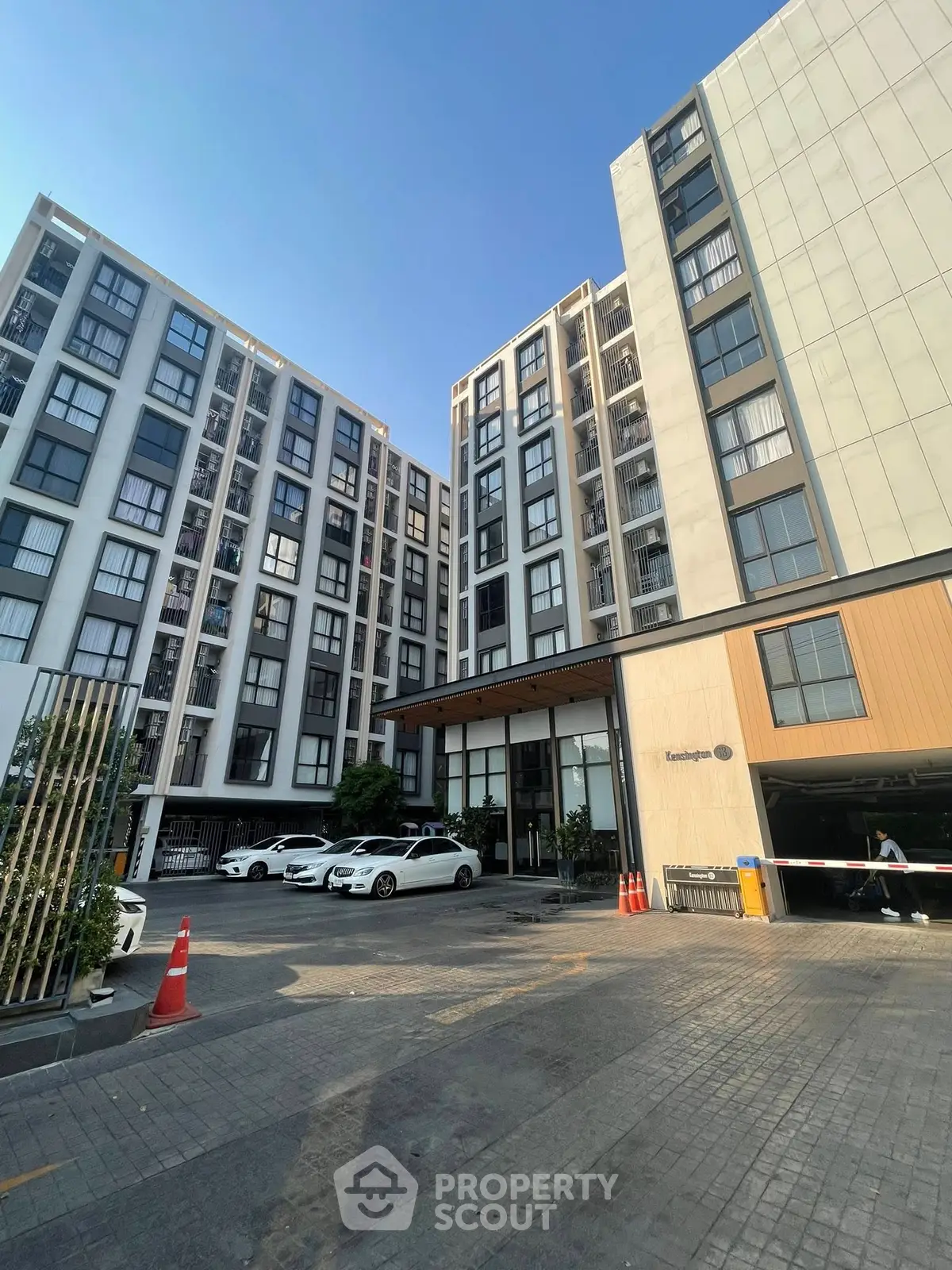 Modern apartment building exterior with parking area and clear blue sky.