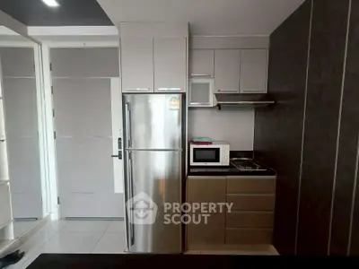 Modern compact kitchen with stainless steel fridge and microwave in sleek apartment.