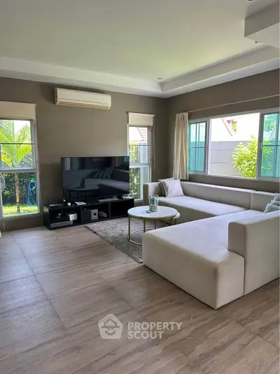 Spacious living room with modern sectional sofa and large windows offering garden views.