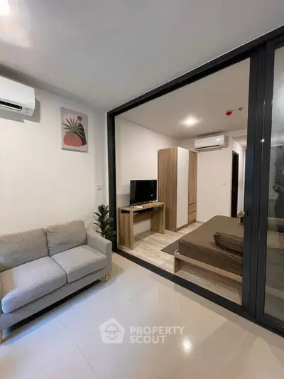 Modern studio apartment with cozy living area and bedroom separated by glass partition.
