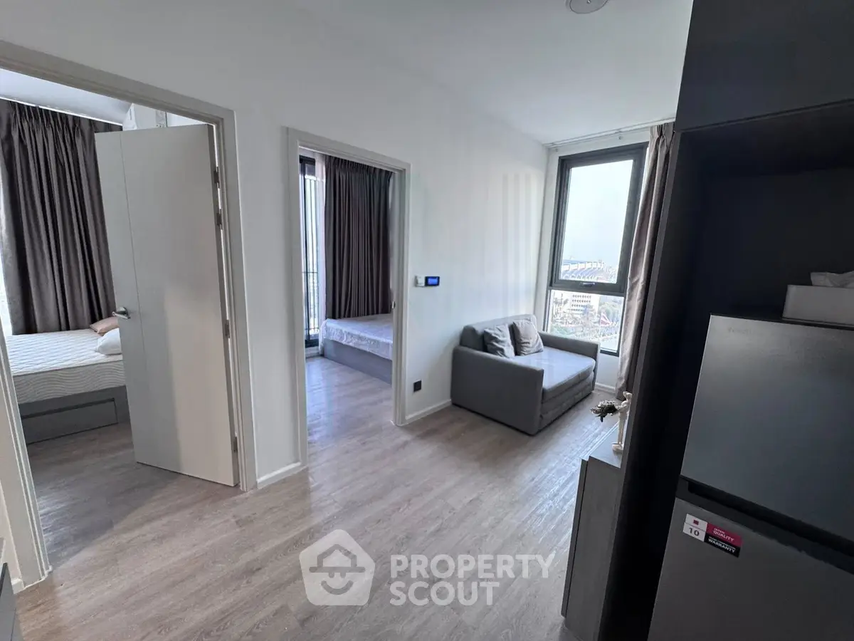 Modern apartment interior with two bedrooms and cozy seating area, featuring large windows and stylish flooring.