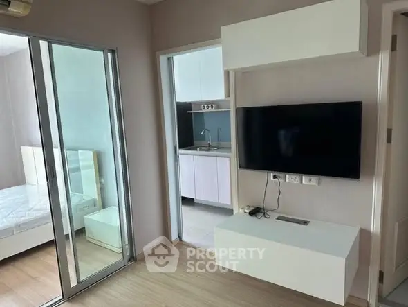 Modern apartment interior with sleek TV setup and sliding glass doors to bedroom.