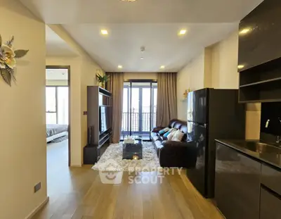 Modern open-plan living room with sleek kitchen and balcony access, featuring hardwood floors and contemporary decor.