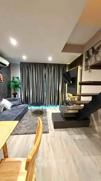 Modern living room with stylish decor and staircase, featuring cozy seating and large windows.