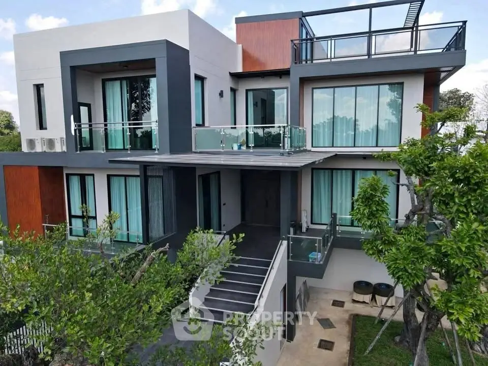 Modern luxury home with large windows and spacious balconies surrounded by lush greenery.