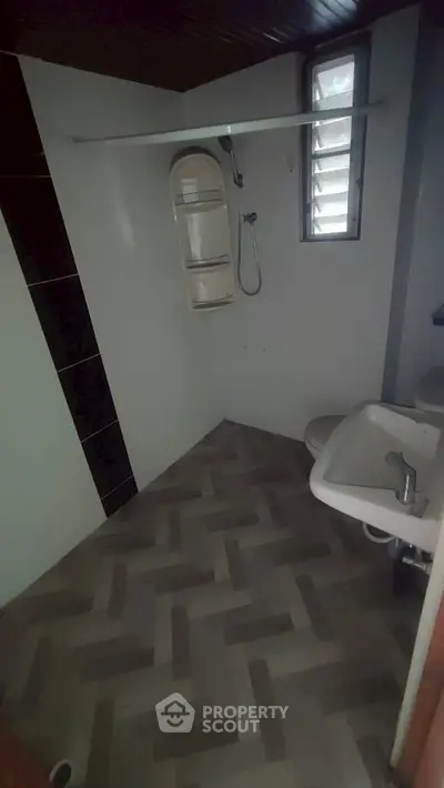 Compact bathroom with modern fixtures and herringbone tile flooring, featuring a shower and small window.