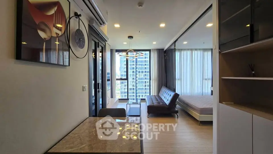 Modern studio apartment with open layout, featuring a stylish living area and large windows with city views.