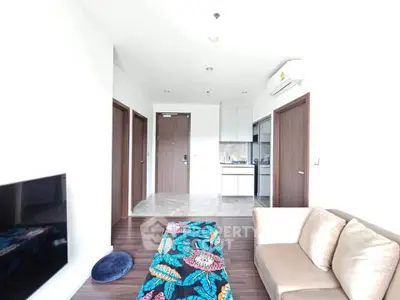 Modern living room with cozy sofa, vibrant rug, and compact kitchen in open layout apartment.