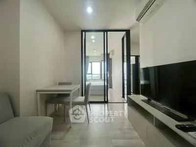 Modern living room with sleek furniture and glass partition leading to bedroom, featuring a minimalist design.