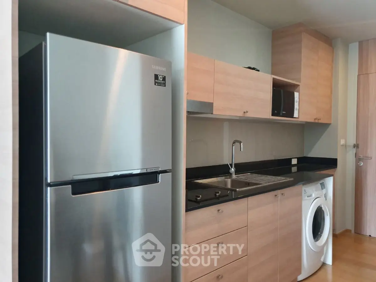 Modern kitchen with sleek appliances and wooden cabinetry, featuring a fridge and washing machine.