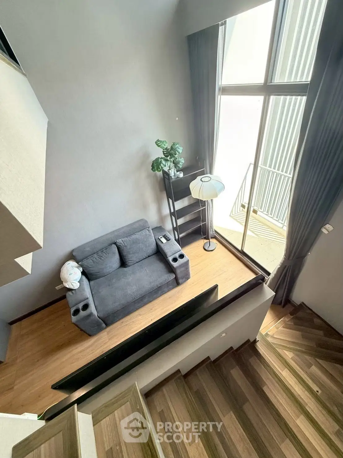 Modern loft-style living room with high ceilings and large windows, featuring a cozy sofa and stylish decor.